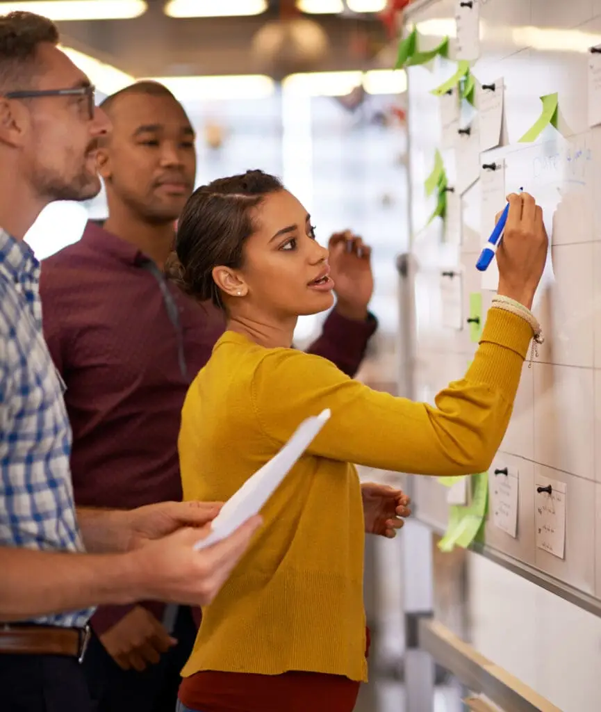 Woman, focus and brainstorm on whiteboard or marketing presentation or male employees and in office. Coach, lady trainer and man workers or flip chart or business project and workplace meeting